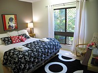 Rainforest Mission Beach Apartments - main bedroom, queen bed, white linen and palm trees through the windows.